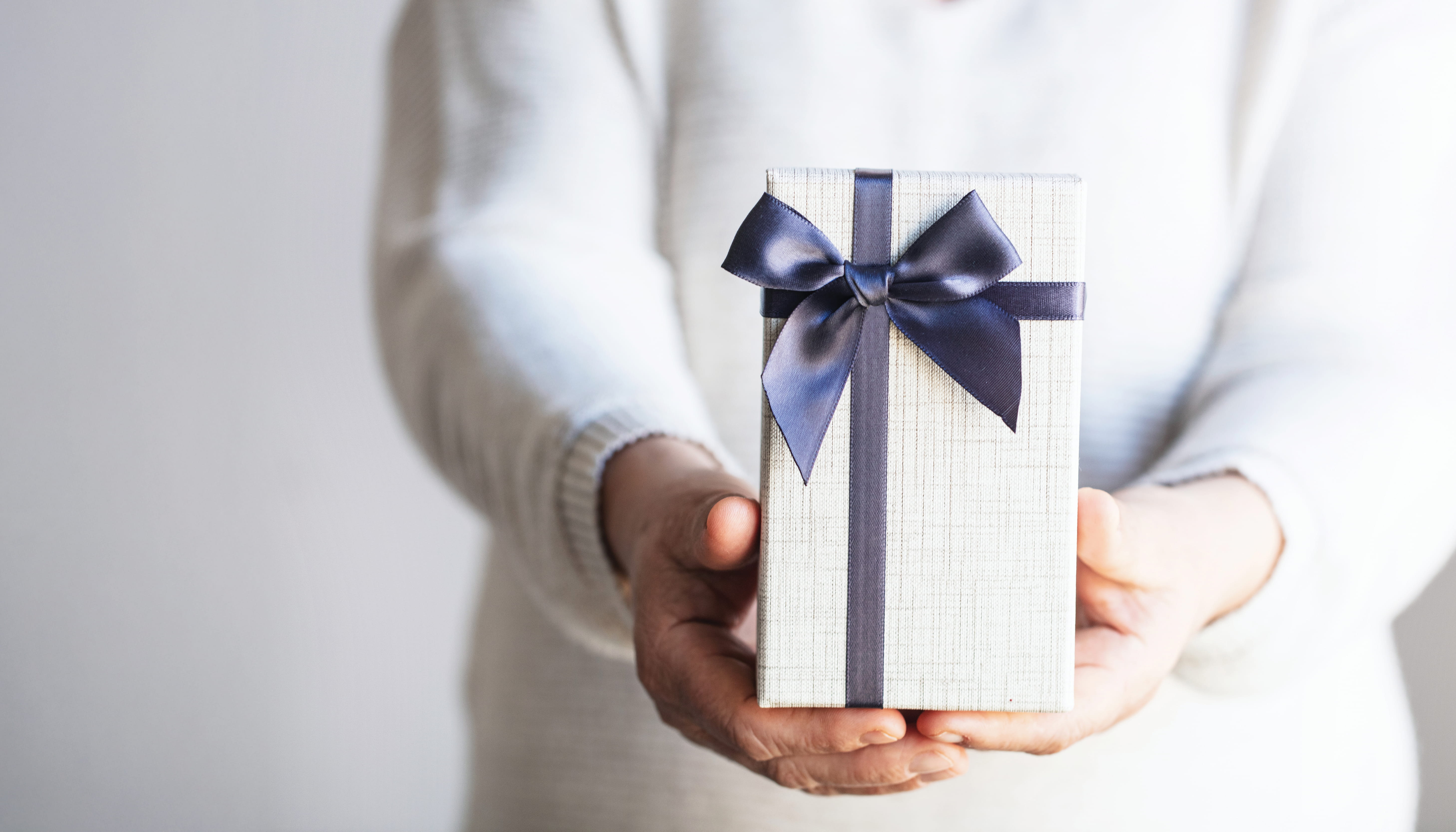 Hands offering a wrapped gift box with a navy ribbon.
