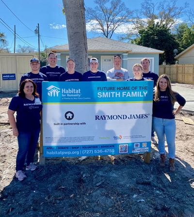 Raymond James volunteer pose by Habitat sign that says "Future home of the Smith family"