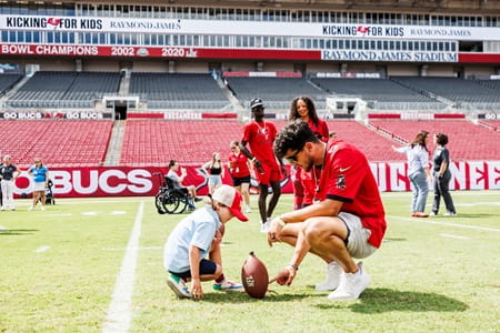 Bucs punter Jake Camarda hold football for young boy to kick
