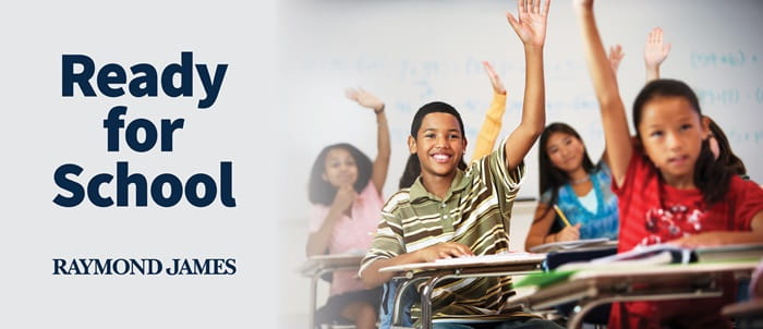 Students in classroom raise their hands. Text on banner says "Ready for School Raymond James"